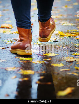 Spaziergang auf dem nassen Bürgersteig. Ansicht von hinten auf den Füßen einer Frau zu Fuß entlang der Asphalt mit Pfützen im Regen. Paar Schuh auf glatter Straße in t Stockfoto