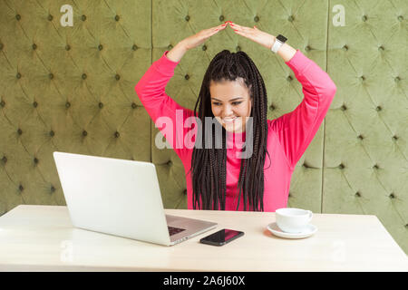 Ich bin in Sicherheit. Portrait kindlicher junge Mädchen mit schwarzen dreadlocks Frisur in rosa Bluse Sitzen im Büro und die Hand die obere Hand, Makin Stockfoto