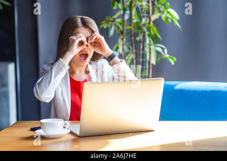 Portrait von überrascht schöne stilvolle Brünette junge Frau in Gläsern sitzen mit Fernglas Geste auf Augen und suchen mit entsetzten Gesicht. ind Stockfoto