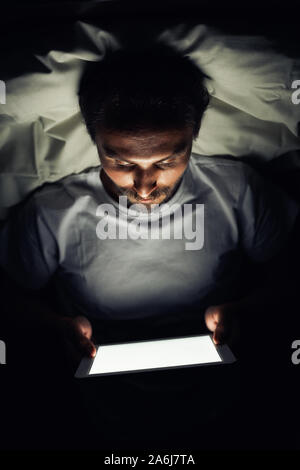 Junge stattlich und müde Mann mit einem Bart kann nicht schlafen und ist etwas aufpassen auf seinem Tablet in der Nacht. Stockfoto