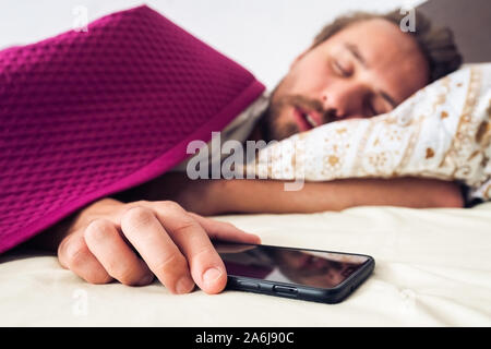Schlafen jungen gutaussehenden Mann, während sein Handy zu halten. Bildschirm auf dem Telefon ist ausgeschaltet Stockfoto
