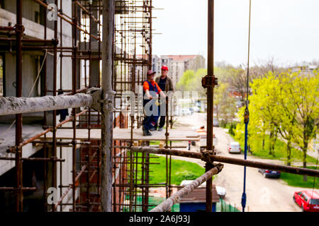 Gerüst ist gegen Gebäude platziert. Chef ist, beaufsichtigt von der Plattform über Baustelle. Stockfoto