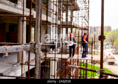 Gerüst ist gegen Gebäude platziert. Chef ist, beaufsichtigt von der Plattform über Baustelle. Stockfoto