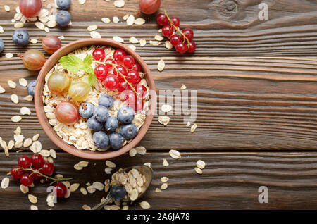 Flach auf Hafer in Ton Schüssel mit Beeren auf hölzernen Tisch Stockfoto