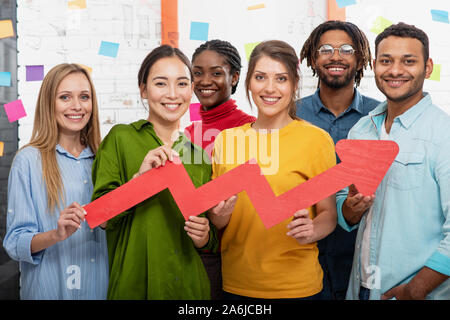 Junge fröhlich-bunten Business Team eine rote statistische Pfeil gedrückt halten. Konzept der wachsenden, erfolgreichen und Gewinn Stockfoto