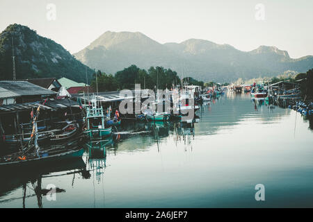 Malerischer Blick auf ein rustikales Fischerdorf an der Küste mit traditionellen Holzbooten, die entlang eines ruhigen Flusskanals mit Bergen angelegt sind. Stockfoto