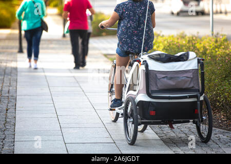 Eine unbekannte Frau auf einem Fahrrad mit einem Baby Stroller am Fahrrad befestigt. Stockfoto