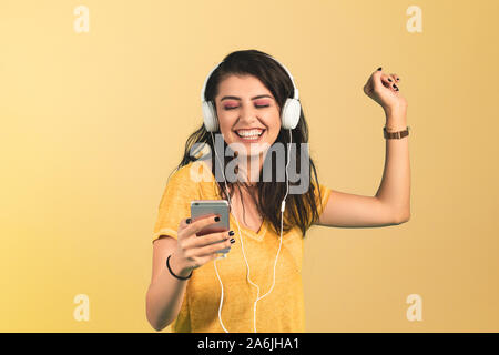 Junge Frau hört Musik mit Smartphone auf gelben Hintergrund. Stockfoto