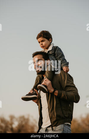 Gerne Vater Sohn Fahrt auf seinen Schultern während des Gehens im Herbst Park. Stockfoto