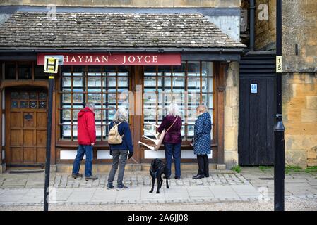 Drei Frauen und ein Mann an der Eigenschaft in einem Immobilienmakler Fenster auf der High Street Broadway Worcestershire England UK angezeigt, Stockfoto