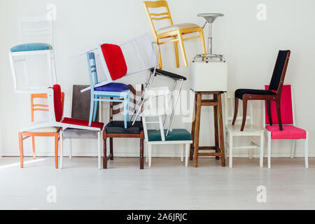 Viele verschiedene Stühle in verschiedenen Farben stehen an der weißen Wand Stockfoto
