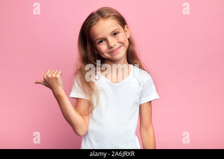 Portrait von positiven Happy girl beiseite etwas verweisen, zeigt in der linken über rosa Hintergrund isoliert, Körpersprache, sehen Sie hier, auf diese Weise, bitte Stockfoto