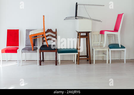 Viele verschiedene Stühle in verschiedenen Farben stehen an der weißen Wand Stockfoto
