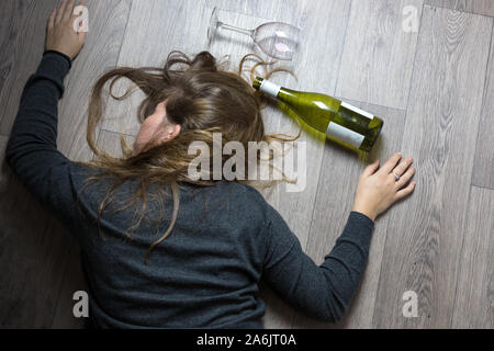 Betrunkene alkoholischen junge Mädchen auf dem Boden liegend Übelkeit durch das Trinken von Rotwein, leeres Glas und Flasche Stockfoto