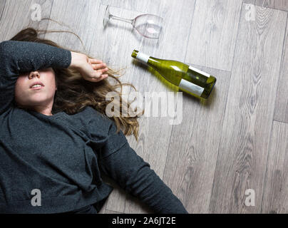 Betrunkene alkoholischen junge Mädchen auf dem Boden liegend Übelkeit durch das Trinken von Rotwein, leeres Glas und Flasche Stockfoto