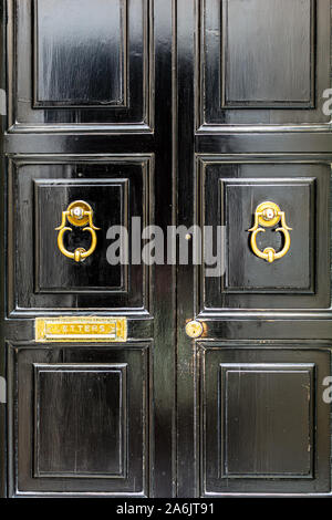 Schwarze hölzerne Tür mit goldenen Jahrgang kunstvoll geformten ring Klopfer und Mailslot Letterbox. Schwarze Tür mit goldenen Hardware. Stockfoto