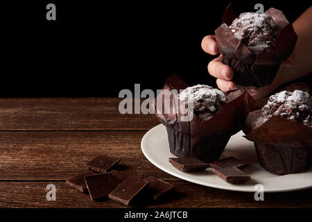 Noch immer leben mit weißen Porzellanteller und Schokolade Muffin mit Zucker auf alten hölzernen Tisch. Frau Hand dienen oder ein Dessert. Mit schwarz Zurück Stockfoto