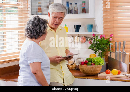 Asiatische senior Paar mit Tablet-PC zu suchen Menü Rezept und Art von Gemüse in der Küche zu Hause. Senior mit Technologie lfiestyle. Altern mit Stockfoto