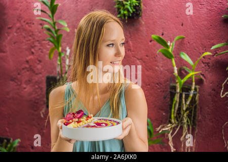 Junge Frau in ein mediterranes Frühstück, isst Gesund tropisches Frühstück, smoothie Schüssel mit tropischen Früchten, mit einem Muster von eingerichtet Stockfoto