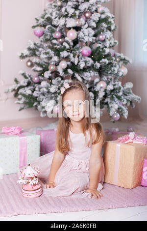 Neues Jahr 2020! Das Konzept von Weihnachten, Feiertage und Kindheit. Ein kleines Mädchen in einem rosa Kleid hält eine musikalische Spielzeug Karussell in der Nähe der Weihnachtsbaum. Stockfoto