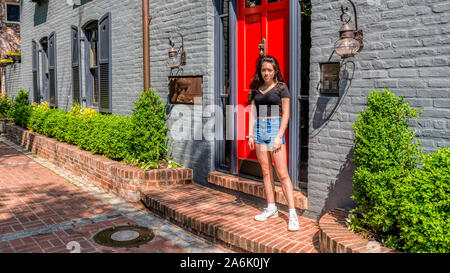 Asiatische jugendlich in Shorts und Turnschuhen stand vor der Tür der bunten Backsteinhäuser holding Jacke Stockfoto