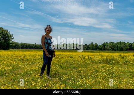 Asiatische Frau mit Sonnenbrille im großen Feld mit gelben Blumen und Bäume im Hintergrund Stockfoto