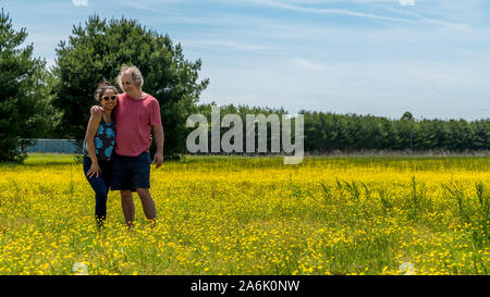 Paar stehend in das große Feld mit gelben Blumen und Bäume im Hintergrund auf der Suche nach Fotograf Stockfoto