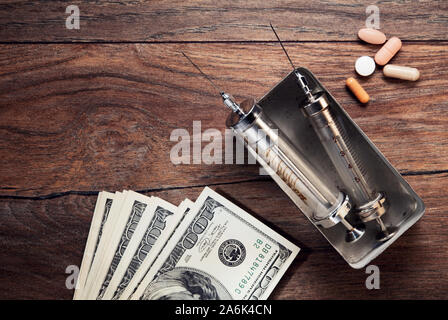 Vintage Spritzen, medizinische Pillen und Dollarscheine auf hölzernen Tisch. Konzept der Gesundheitsbranche, Geld und Drogen. Stockfoto