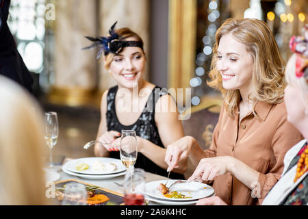 Elegant gekleidete Frauen mit einem festlichen Abendessen in einem gut versorgten Tisch mit leckeren Gerichten während Silvester im luxuriösen Restaurant Stockfoto