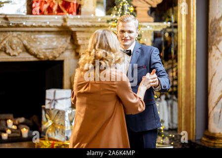 Junge gut gekleidete Paare tanzen in der Nähe der Weihnachtsbaum im Neuen Jahr Feier in den wunderschön dekorierten Home Stockfoto