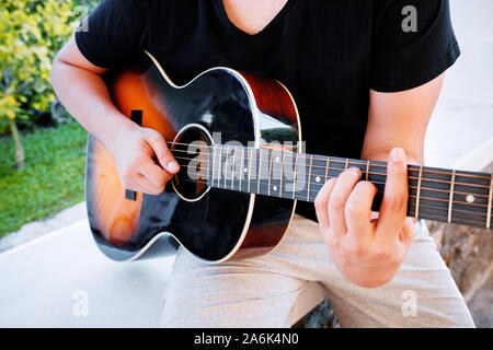 Hände von einem jungen Mann spielen akustische Gitarre in den Garten. Nähe zu sehen. Stockfoto