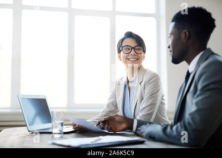 Portrait von lächelnden jungen Geschäftsfrau Arbeiten an Dokumenten, während in der Sitzung Tabelle mit Kollegen oder Partner sitzen, Platz kopieren Stockfoto