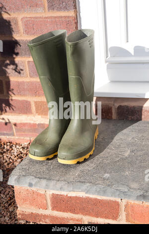 Paar grüne wellington Stiefel (Vorderansicht) isoliert im Freien vor der Haustür von britischen Wohnimmobilien nach einem Spaziergang in der Herbstsonne. Stockfoto