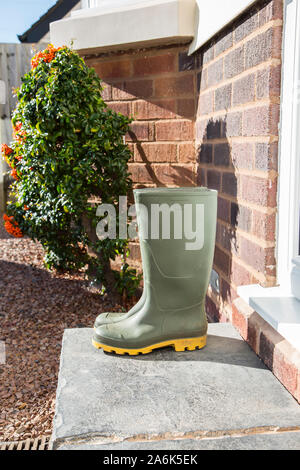 Paar sonnigen, grünen Gummistiefel (Seitenansicht) isoliert im Freien auf einem britischen Haustür nach einem Spaziergang im Herbst Sonnenschein. Stockfoto