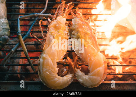 In der Nähe der Flamme gegrillten Hummer, halbiert und Grillen auf dem Grillplatz im Freien an einem Street Food Market Stall-frische Meeresfrüchte Abendessen am Strand Frühstücksbuffet, einschließlich Riesengarnelen und Fisch kochen am offenen Grill Stockfoto