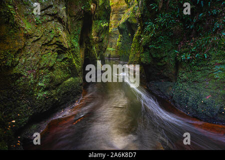 Devil's Kanzel in Finnich Glen in der Nähe von Glasgow, Schottland, Großbritannien. Schlucht im Wald mit fließendem Wasser und Felsen mit grünem Wachstum von morgen Licht beleuchtet. Stockfoto