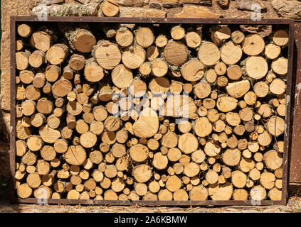 Stapel von cut Protokolle und Niederlassungen für Brennholz in Rahmen von Stein an der Wand des alten Hauses Stockfoto