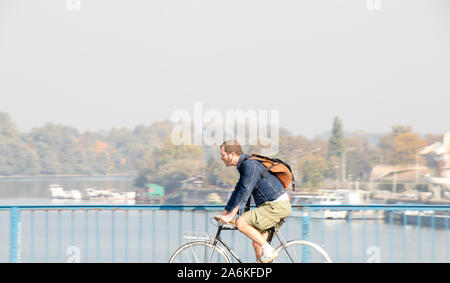 Belgrad, Serbien - 17. Oktober 2019: Eine rothaarige Mann reiten Fahrrad auf city Street Bridge mit Ufer Landschaft im Hintergrund Stockfoto