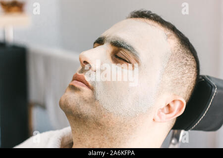 Männliche Hautpflege im Schönheitssalon. Anwendung Ton reinigende Maske auf das Gesicht eines Mannes Stockfoto