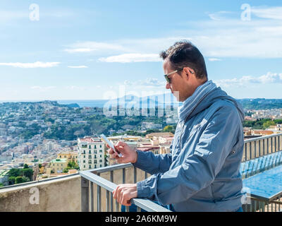 Junger Mann mit Sonnenbrille auf der Terrasse, während Sie sein Smartphone Stockfoto