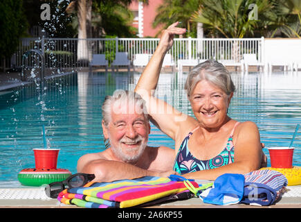 Zwei ältere Menschen Lächeln und genießt freien Zeit im Pool. Sonne im Gesicht. Floating Gläser mit Strohhalm. Serene Ruhestand Tage Stockfoto