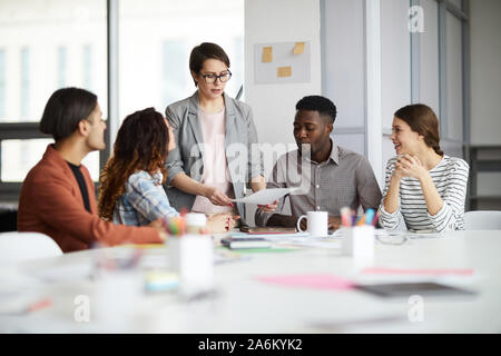 Vielfältige Gruppe junger Geschäftsleute diskutieren Projekt am Tisch sitzen in modernen Büro, auf weibliche Manager übergabe Dokumente, kopieren Raum konzentrieren Stockfoto