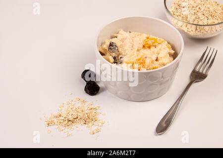 Salat von Apple, Orange, oat Hopfen und Pflaumen mit Honig in eine weiße Platte auf einem weißen Hintergrund. Stockfoto