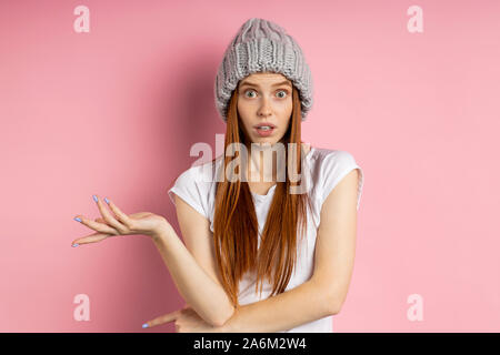 Betrübt und ratlos Frau mit roten Haaren sommersprossige Haut, Kamera mit Empörung, tragen Strickmütze, t shirt über rosa Hintergrund isoliert. Stockfoto