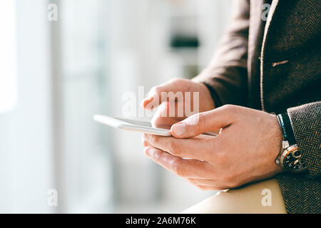 Junge elegante Geschäftsmann mit Armbanduhr holding Smartphone während texting Stockfoto