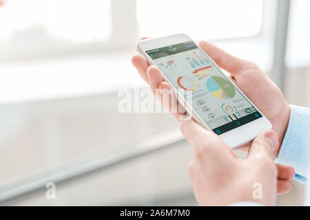 Junge Wirtschaftswissenschaftler oder Financial Analyst smartphone Holding mit Karten und Diagramme Stockfoto