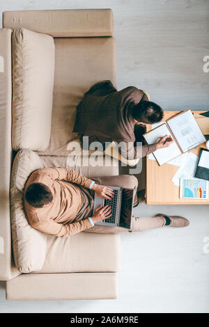 Junge broker Notizen zu machen, während seine Kollegen mit Laptop arbeiten über Projekt Stockfoto