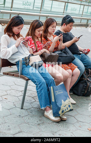 Barcelona Spanien,Katalonien Passeig de Gracia,Einkaufsviertel,Boulevard Bank,sitzen,Asiatisch,Junge,Mädchen,Teenager,Freunde,mit Smartphones,ohne Surro Stockfoto