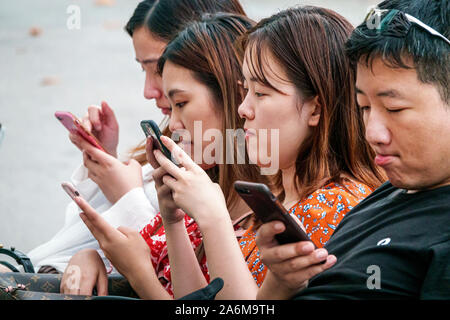 Barcelona Spanien,Katalonien Passeig de Gracia,Einkaufsviertel,Boulevard Bank,sitzen,Asiatisch,Junge,Mädchen,Teenager,Freunde,mit Smartphones,ohne Surro Stockfoto