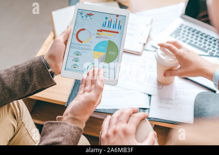 Junge männliche Wirtschaftswissenschaftler mit Touchpad auf finanzielle Diagramm am Bildschirm Stockfoto